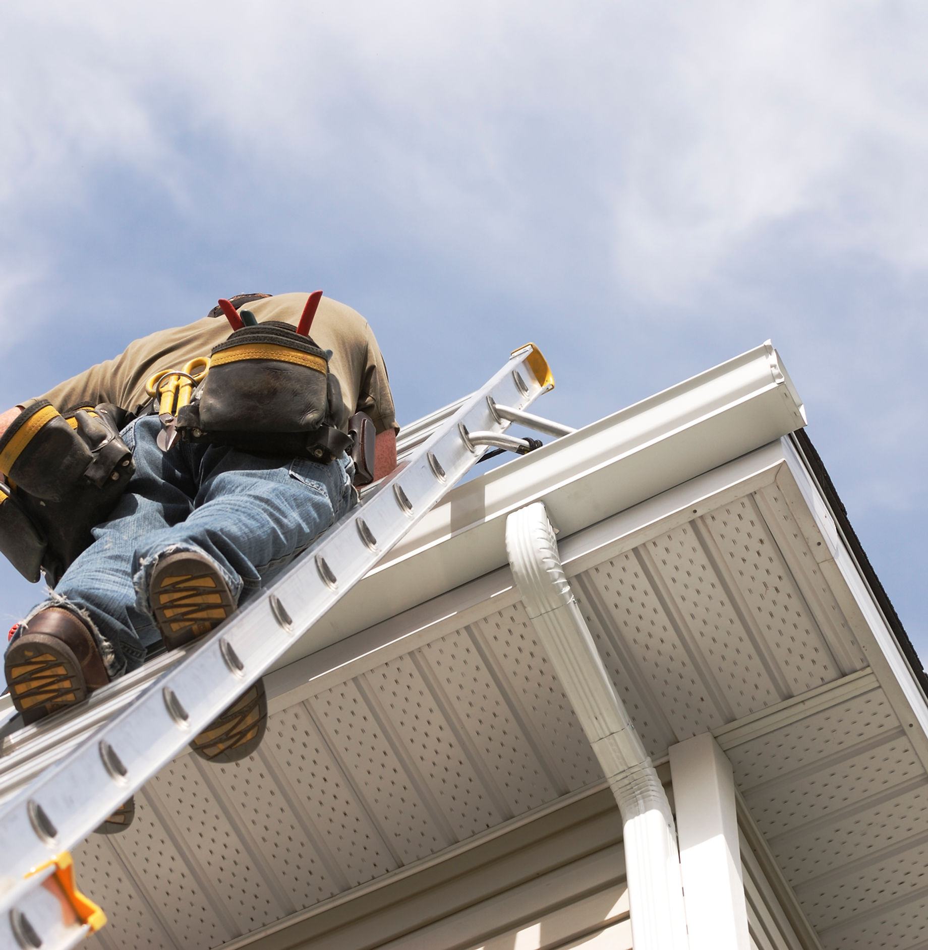 A GreenBros roofer working from a ladder at the gutter line